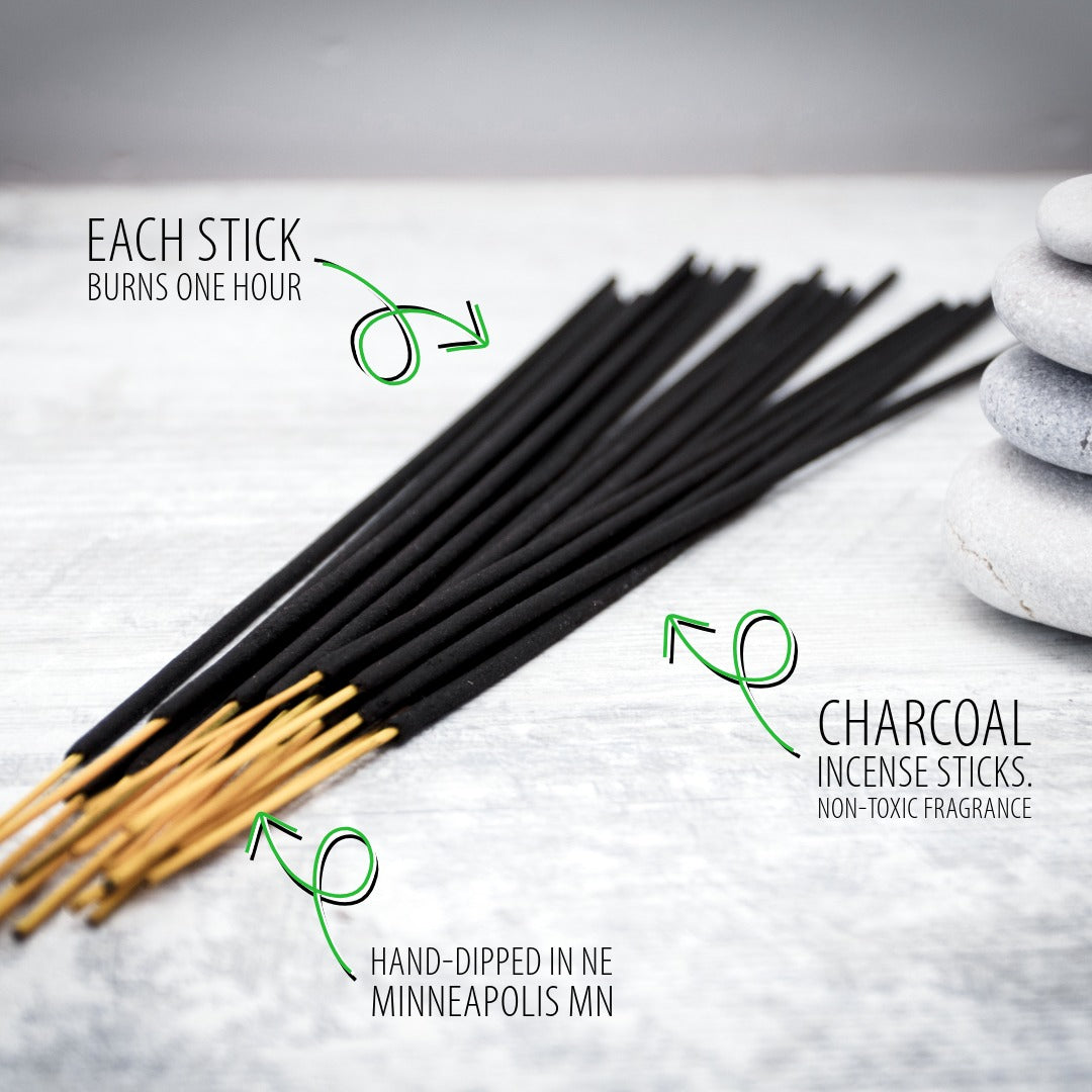 A fan of black charcoal incense sticks with tan wooden tips arranged on a light stone surface, with green text callouts explaining that each stick burns one hour and that the sticks are hand-dipped in Minneapolis MN charcoal incense.