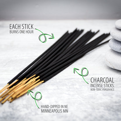 A fan of black charcoal incense sticks with tan wooden tips arranged on a light stone surface, with green text callouts explaining that each stick burns one hour and that the sticks are hand-dipped in Minneapolis MN charcoal incense.