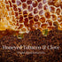 Honeycomb dripping amber honey onto a bed of loose tobacco leaf, with the label overlaid in white