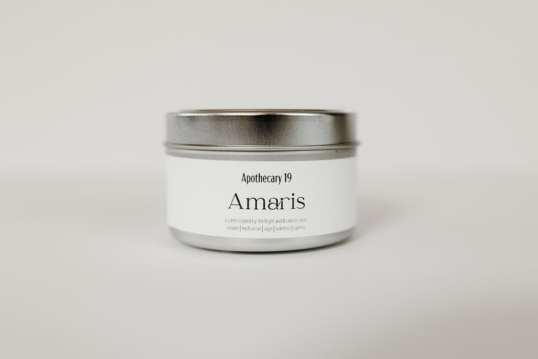 Silver candle tin with lid. White rectangular label that reads Amaris and Apothecary 19.
